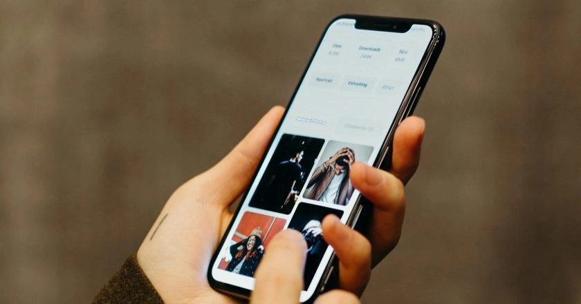 A person holding a smartphone and scrolling through a photo gallery app that displays four images, including people and portraits, with a blurred background.