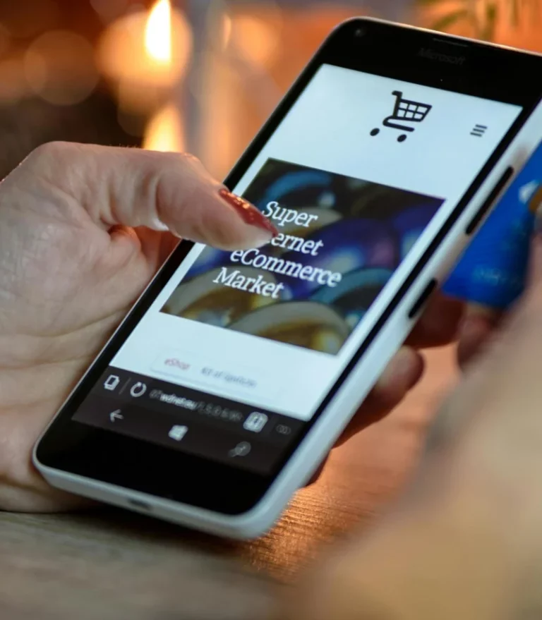 A person holding a smartphone with an online shopping site open on the screen and a blue credit card in hand, suggesting they are making an online purchase.