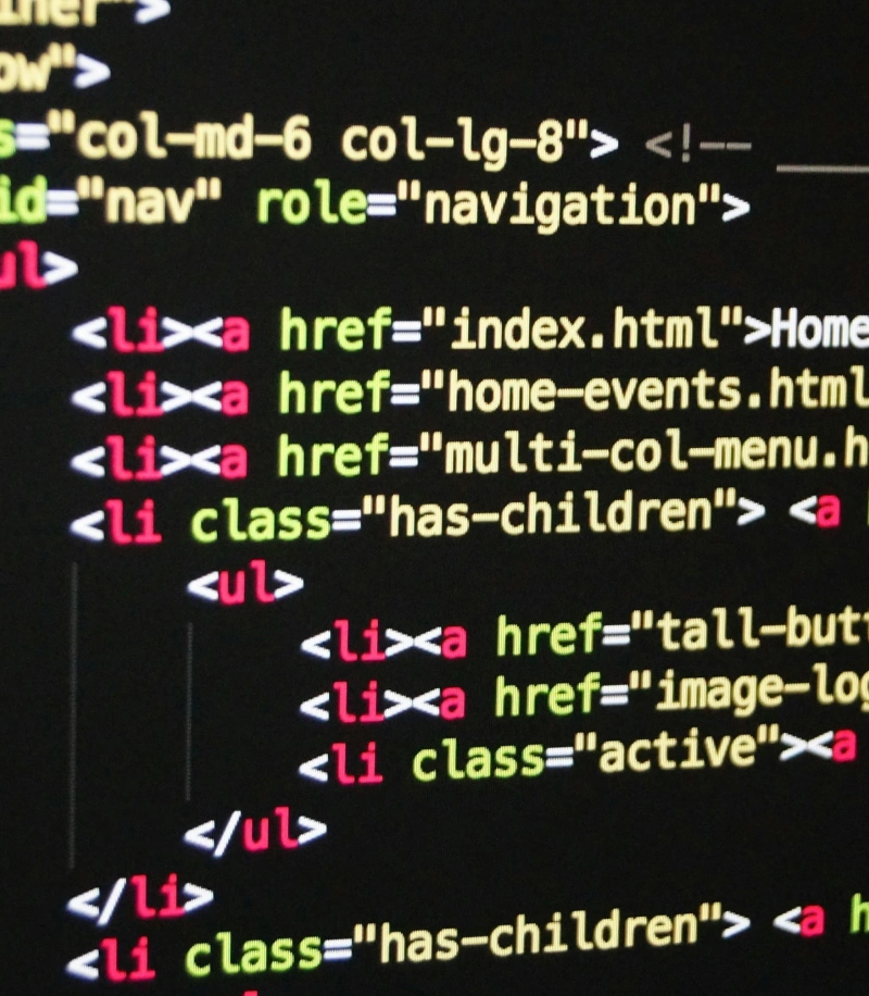 Close-up of a computer screen displaying colorful HTML code, including elements like "ul", "li", "a", and various classes and href attributes on a black background.