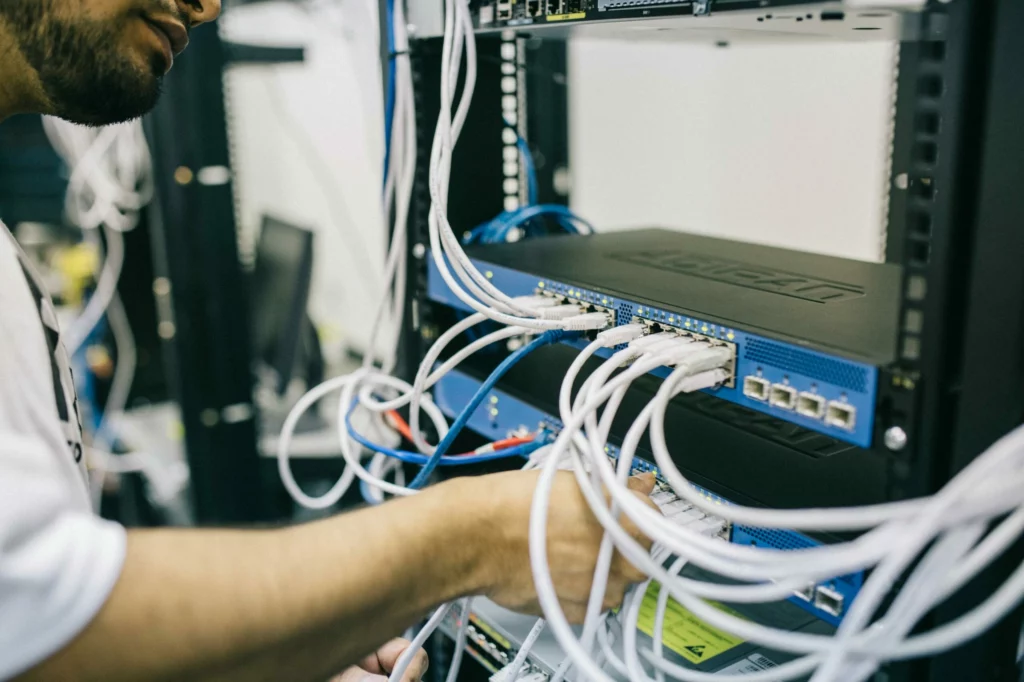 A person connects and arranges white network cables on a rack-mounted server or network switch in a data center or server room.
