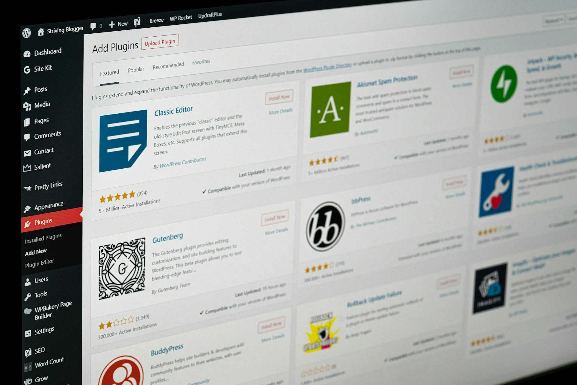 A computer screen showing the WordPress dashboard with the “Add Plugins” page open, displaying a list of available plugins such as Classic Editor, Gutenberg, BuddyPress, and others.